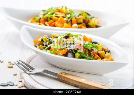 Gemischter Salat aus gebratenem Gemüse mit Rucola und Samen auf Holzgrund Stockfoto