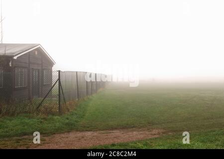 Cottage hinter dem Zaun der Kettenverbindung am nebligen Tag Stockfoto