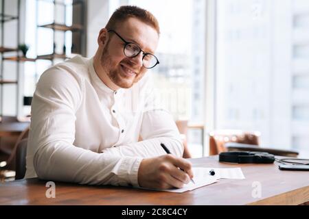 Talentierter junger freiberuflicher Songwriter mit stilvollen Brillen schreibt mit Stift Liednotiz Stockfoto