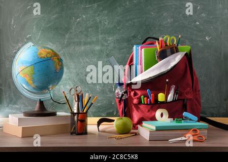 Klasse mit Rucksack mit Schulbedarf auf Holztisch und grünem Kreidetafel Hintergrund Stockfoto