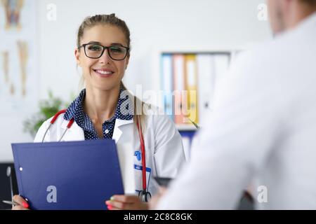 Ärztin lächelt und hält Clipboard in ihren Händen. Stockfoto