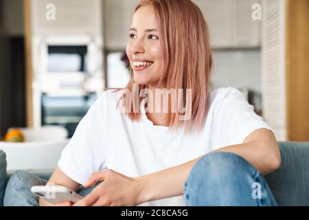 Bild von fröhlichen hübsche Frau mit rosa Haar mit Handy, während auf dem Sofa zu Hause ruhen Stockfoto