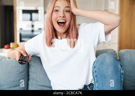 Schöne fröhliche junge attraktive Frau, die sich auf einer Couch im Wohnzimmer entspannt und fernsieht Stockfoto