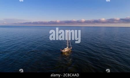 Luftaufnahme eines Segelbootes in der Mitte des Meeres. Boot mit gewickelten Segeln schwimmt auf einem ruhigen Meer. Sonnenaufgang im Sommer oder Frühling. Stockfoto