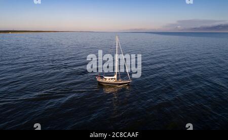 Luftaufnahme eines Segelbootes in der Mitte des Meeres. Boot mit gewickelten Segeln schwimmt auf einem ruhigen Meer. Sonnenaufgang im Sommer oder Frühling. Stockfoto