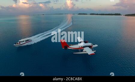 Wasserflugzeug während Sonnenuntergang Luftaufnahmen. Weiß schwarz rot Wasserflugzeug dockt in der Mitte des Indischen Ozeans, Speed boat vorbeifährt Stockfoto