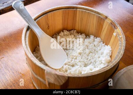 Lecker gekochter Reis in einer großen Holzschüssel, verzehrfertig mit weißem Reisspatel Löffel am Restauranttisch, Nahaufnahme, Lifestyle. Stockfoto