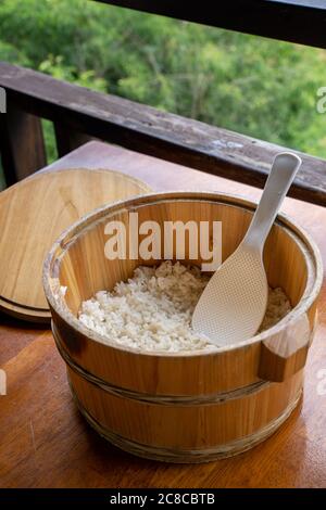 Lecker gekochter Reis in einer großen Holzschüssel, verzehrfertig mit weißem Reisspatel Löffel am Restauranttisch, Nahaufnahme, Lifestyle. Stockfoto