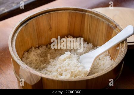 Lecker gekochter Reis in einer großen Holzschüssel, verzehrfertig mit weißem Reisspatel Löffel am Restauranttisch, Nahaufnahme, Lifestyle. Stockfoto