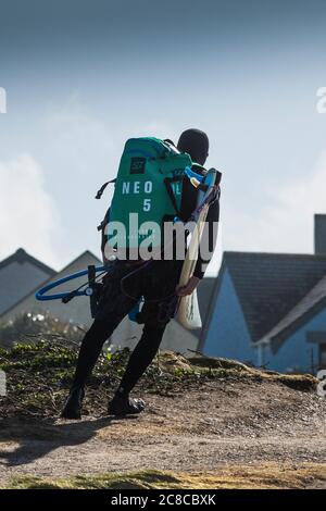 Ein Kite-Boarder, der seine Ausrüstung mit sich führt und mit dem Mühe kämpft, in Fistral in Newquay in Cornwall in sehr starke Winde zu gehen. Stockfoto