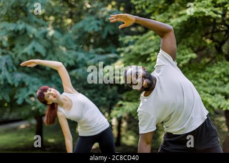 Aktive gesunde Paar, African guy und kaukasischen Mädchen, gemeinsam im Freien zu arbeiten, Stretching-Übungen auf dem Gras. Sport und Fitness Stockfoto