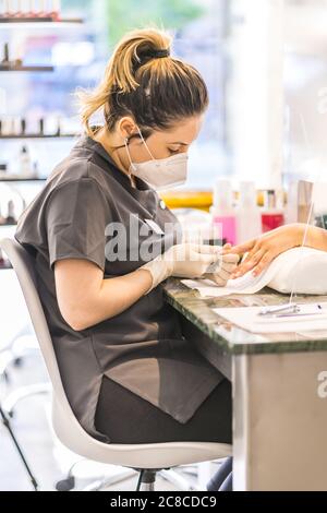 Seichte Fokus vertikale Aufnahme von Hispanic weibliche Nagelkünstler tragen Maske Malerei Client Nägel Stockfoto