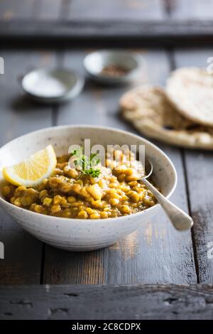 Linsen Dal. Vegan freundliches Dhal serviert mit Zitronen- und Kräutergarnieren in einem rustikalen Gericht mit Fladenbrot Stockfoto