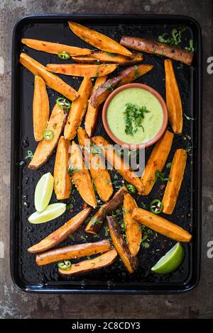 Süßkartoffelkeile mit Cajun-Gewürzen, Koriandersauce und Limettenkeilen Stockfoto