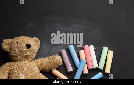 Brauner Teddybär und bunte Buntstifte auf schwarzem Kreidetafel, zurück zur Schule Stockfoto