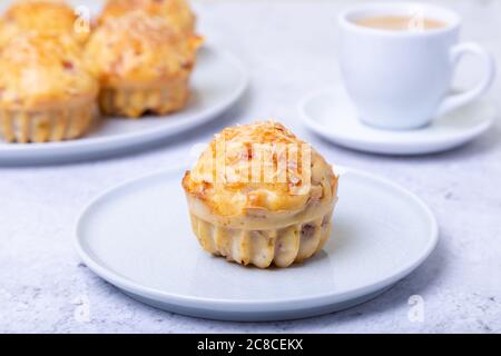 Muffins mit Schinken und Käse. Hausgemachtes Backen. Im Hintergrund ist ein Teller mit Muffins und eine Tasse Kaffee. Nahaufnahme. Stockfoto