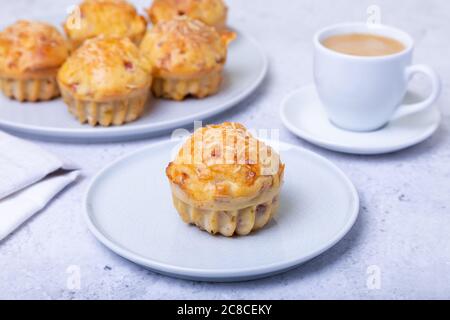 Muffins mit Schinken und Käse. Hausgemachtes Backen. Im Hintergrund ist ein Teller mit Muffins und eine Tasse Kaffee. Nahaufnahme. Stockfoto