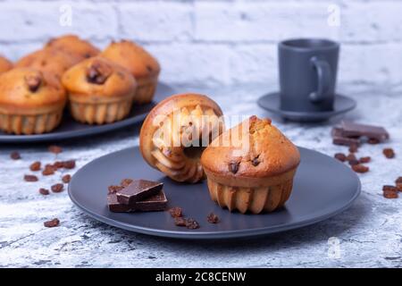 Muffins mit Schokolade und Rosinen. Hausgemachtes Backen. Im Hintergrund ist ein Teller mit Muffins und eine Tasse Kaffee. Nahaufnahme. Stockfoto