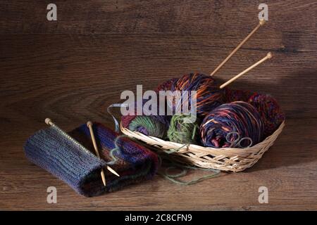 Stricken und Wolle in einem Korb auf Holzoberfläche Stockfoto