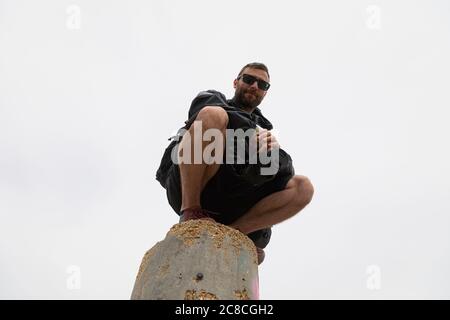 Ein junger Mann beobachtet, gekauert, mit seiner Kamera in der Hand, von der Spitze des geodätischen Punktes des Moncayo, dem höchsten Berg des Iberischen Systems, in Stockfoto