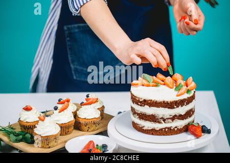 Zugeschnittenes Bild von Frau Hände Dekoration Cupcakes mit Erdbeeren. Stockfoto