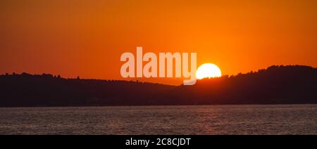 Sonnenuntergang hinter Hügeln und Meer Stockfoto