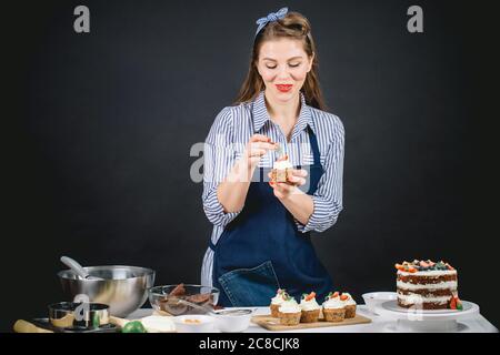 Glückliche junge Frau Vorbereitung für Geburtstagsfeier, Dekoration cremige Topping Cupcakes mit Beeren auf schwarzem Hintergrund. Stockfoto