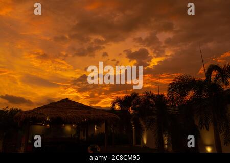 Schöner orange feuriger Sonnenuntergang in den Tropen. Straßendach von Heu, neben dem Pool und mit Blick auf das Reisfeld Stockfoto