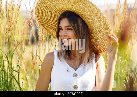 Porträt einer jungen lächelnden Frau, die einen großen Strohhut im Freien trägt Stockfoto