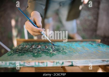 Weibliche Hand halten Pinsel mit blauer Farbe über bemalten Leinwand Stockfoto