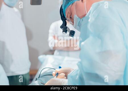 Chirurg, der kosmetische Chirurgie an der Nase im Operationssaal des Krankenhauses durchführt. Chirurg in Maske mit chirurgischen Lupen während des medizinischen Eingriffs. Stockfoto