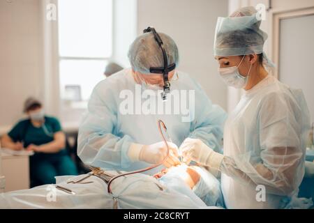 Chirurg, der kosmetische Chirurgie an der Nase im Operationssaal des Krankenhauses durchführt. Chirurg in Maske trägt chirurgische Lupen während des medizinischen Eingriffs. Nasenaugment Stockfoto