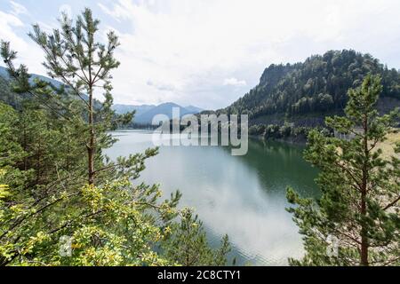 Lenggries, Deutschland. Juli 2020. Eine leichte Spiegelung der Berge ist im Wasser des Sylvenstein Stausees zu sehen. Verschiedene Maßnahmen rund um die tiefen Ausläufe des Stausees verbessern den Betrieb bei hoch- und Niedrigwasser entlang der Isar von Bad Tölz über München bis in den Donauraum Niederbayern. Nach einer Bauzeit von rund fünf Jahren sind die Bauarbeiten mit einem Finanzvolumen im zweistelligen Millionenbereich abgeschlossen. Quelle: Matthias Balk/dpa/Alamy Live News Stockfoto