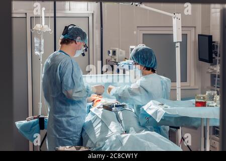 Weitblick eines Teams von vier Chirurgen, die im Dunkeln ODER im Krankenhaus an einem Patienten operieren Stockfoto