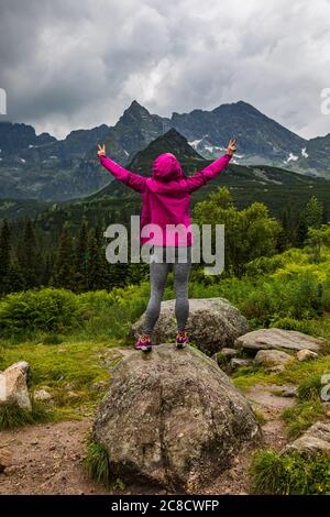 Kapuzenfrau, die im Regen das Tatra-Bergpanorama mit breiten Händen betrachtet - Portrait-Orientierung Stockfoto