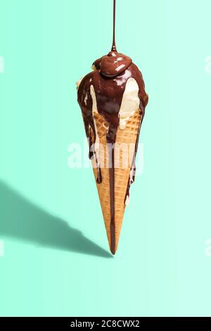 Vanilleeis-Konus mit geschmolzener Schokoladendecke, isoliert auf grünem Minzhintergrund, in hartem Licht. Sommerdessert. Tropfende Schokoladensoße Stockfoto