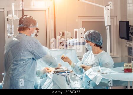 Weitblick eines Teams von vier Chirurgen, die im Dunkeln ODER im Krankenhaus an einem Patienten operieren Stockfoto