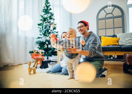 Glückliche Mutter und Vater zeigt Weihnachtskugel Baby in der Nähe Weihnachtsbaum Stockfoto