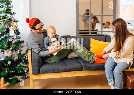 Baby mit Vater auf Sofa und mit digitalen Tablet während Weihnachten. Sohn und Eltern im Wohnzimmer während weihnachten. Stockfoto