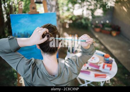 Mädchen machen Haar bun mit Pinsel vor bemalten Leinwand Stockfoto