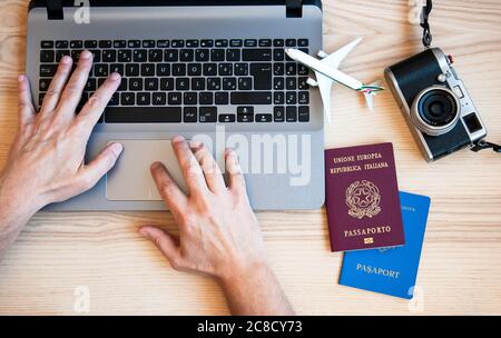 Männliche Hände tippen auf einem modernen Laptop für die Buchung eines Flugzeugs - Mann plant Paar-Tour mit Pässen auf dem Schreibtisch für den Urlaub - andere nationali Stockfoto