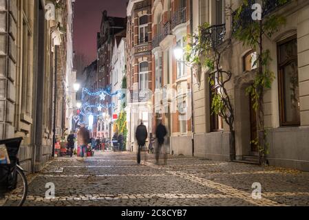 Menschen, die im Winter nachts in einer alten Innenstadt eine gepflasterte Fußgängerzone mit historischen Gebäuden und Restaurants entlang laufen Stockfoto