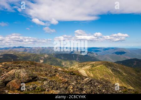 Herrliche Aussicht auf die Berge vom Tschersky Peak. Berggipfel von Khamar-Daban im Sommer vor dem Hintergrund des blauen Himmels und Wolken. Stockfoto