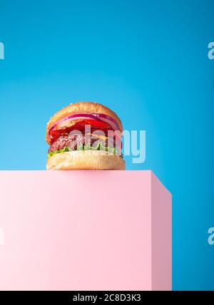 Frischer, saftiger Rindfleisch-Hamburger auf dem Ständer und blauem Hintergrund. Platz für Text kopieren, trendige Hero-Ansicht Stockfoto