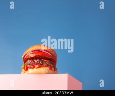 Frischer, saftiger Rindfleisch-Hamburger auf dem Ständer und blauem Hintergrund. Platz für Text kopieren, trendige Hero-Ansicht, horizontal Stockfoto