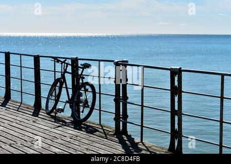 Einzelfahrrad auf Pier mit hellblauem Meer im Sommer. Silhouette des Fahrrads auf Holzboden Stockfoto