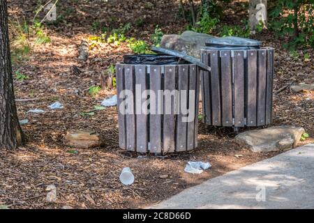 Müll liegt auf dem Boden um zwei Mülltonnen entlang des Weges im Park durch die Wälder, die die Umwelt an einem sonnigen Tag im Sommer verschmutzen Stockfoto