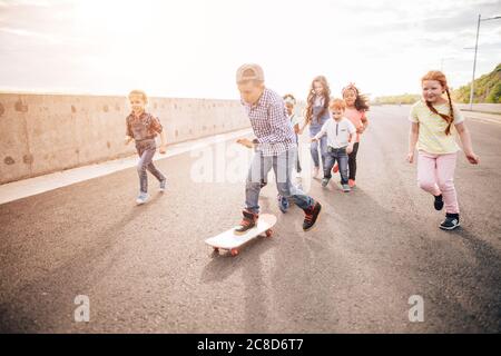 Aktive junge Menschen - Rollerblading, Skateboarding. Ein Junge reitet auf einem Skateboard, die anderen laufen ihm nach. Stockfoto