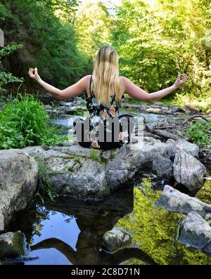 Schöne blonde Frau, die Yoga vor einem Fluss macht Stockfoto