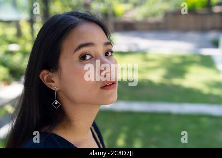 Nahaufnahme einer Frau mit langen Haaren, die im Park auf die Kamera schaut. Stockfoto